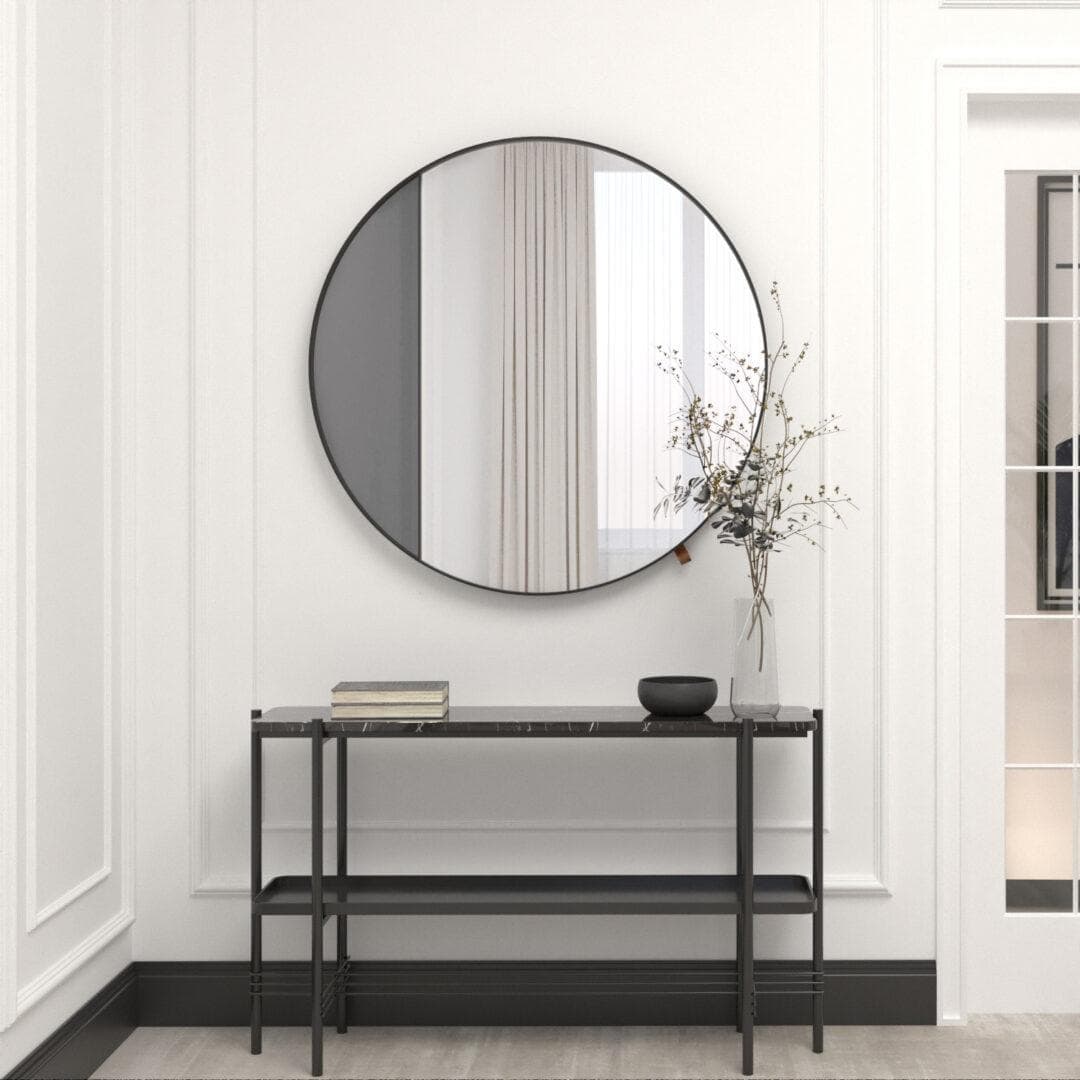 W minimalistycznym przedpokoju znajduje się okrągłe lustro Lustro-100-grafit nad eleganckim czarnym stołem konsolowym z książkami, misą i wazonem z gałęziami. Lustro odbija jasne ściany i szklane drzwi.