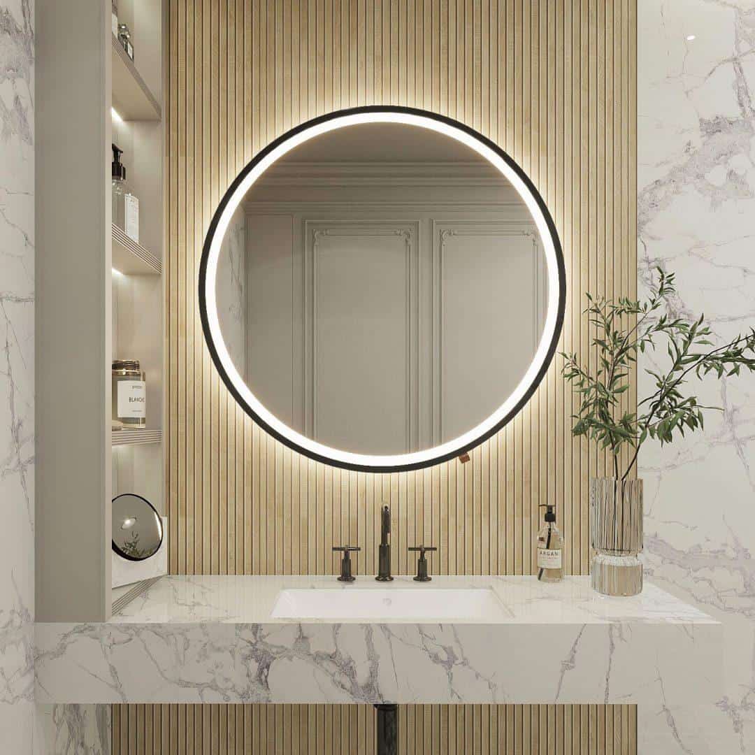 Nowoczesna łazienka z okrągłym podświetlanym lustrem Add-home-Ring-100cm-rama nad marmurową umywalką Rama. Pionowe drewniane panele na ścianie, półki na przybory toaletowe i szklany wazon z zielonymi gałązkami na blacie.