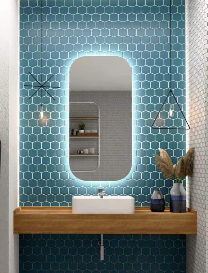 Nowoczesna łazienka z niebieskimi sześciokątnymi płytkami na ścianach, drewnianą pływającą toaletką z białą umywalką, lustrem PROSTOKAT_ZAOKRAGLONY_50X110_WYKADROWANY, dwoma lampami wiszącymi i wazonami z trawą pampasową.