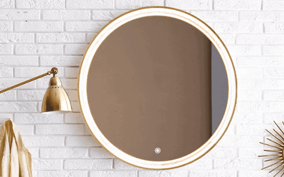 Okrągłe lustro ze złotą ramą wisi na ścianie z białej cegły. Po lewej stronie zamontowano lampę Pitagoras-Perfection-Slim-LED5, a na prawo od lustra częściowo pojawia się dekoracja ścienna w kształcie wybrzuszenia słońca.