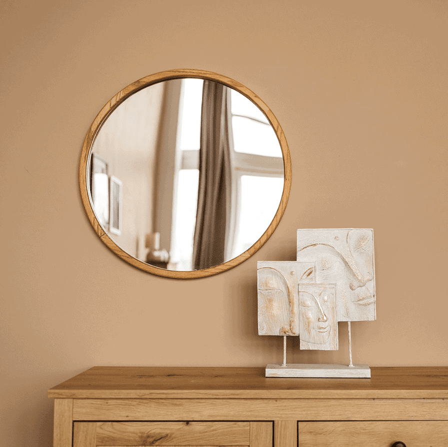 Obraz Pitagoras-Perfection-Slim4.png wisi na beżowej ścianie nad komodą z jasnego drewna. Na komodzie znajduje się biała abstrakcyjna rzeźba z wygrawerowanymi twarzami i kształtami, z oknem i zasłonami odbijającymi się w lustrze.