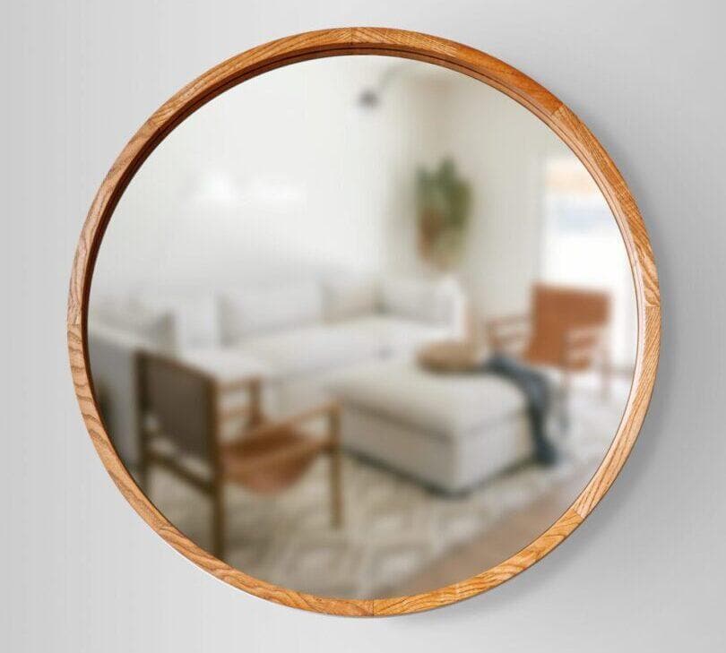 Lustro koniak1-scaled-e1654703870687.jpg pięknie odbija rozmyty obraz nowoczesnego salonu z sofą, krzesłami i rośliną.