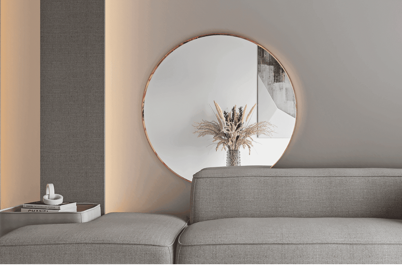 Nowoczesny salon z okrągłym lustrem ściennym miedz.png odbijającym wazon z suszonymi kwiatami, szarą sofą i stolikiem bocznym z tacą i świecą. Neutralne odcienie i delikatne oświetlenie dopełniają przytulną atmosferę.