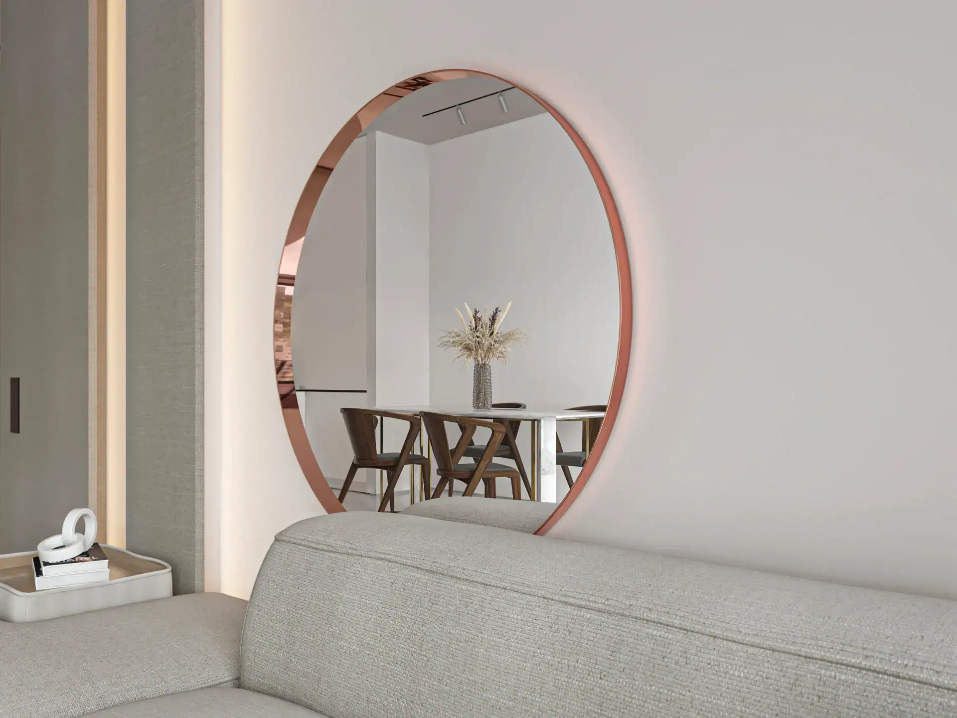 Okrągłe lustro miedz_closeup-scaled-1.webp nad jasnoszarą sofą odbija stół z drewnianymi krzesłami i wazon z suszonymi kwiatami, tworząc nowoczesną, minimalistyczną scenę wnętrza.