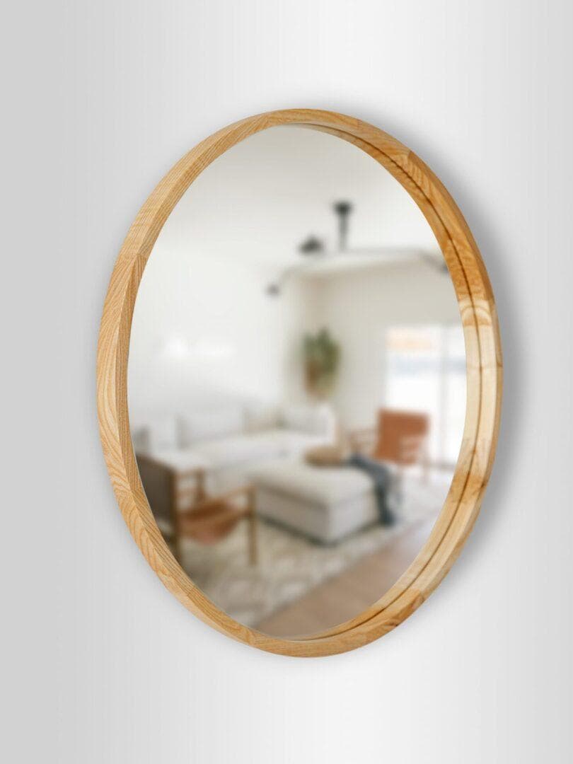 Natural2-scaled-1.jpg wisi na białej ścianie, odbijając rozmazany obraz salonu z sofą, stolikiem kawowym, fotelem i dużym oknem.