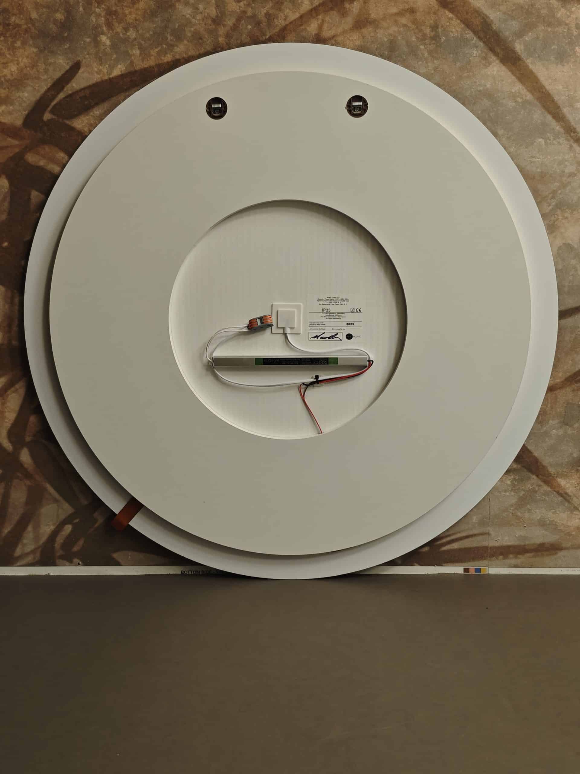 Duże, okrągłe, białe tylne lustro przypomina twarz - z dwoma otworami na śruby jako oczami i otwartą komorą jako ustami - z odsłoniętymi przewodami i komponentami elektronicznymi z tyłu.